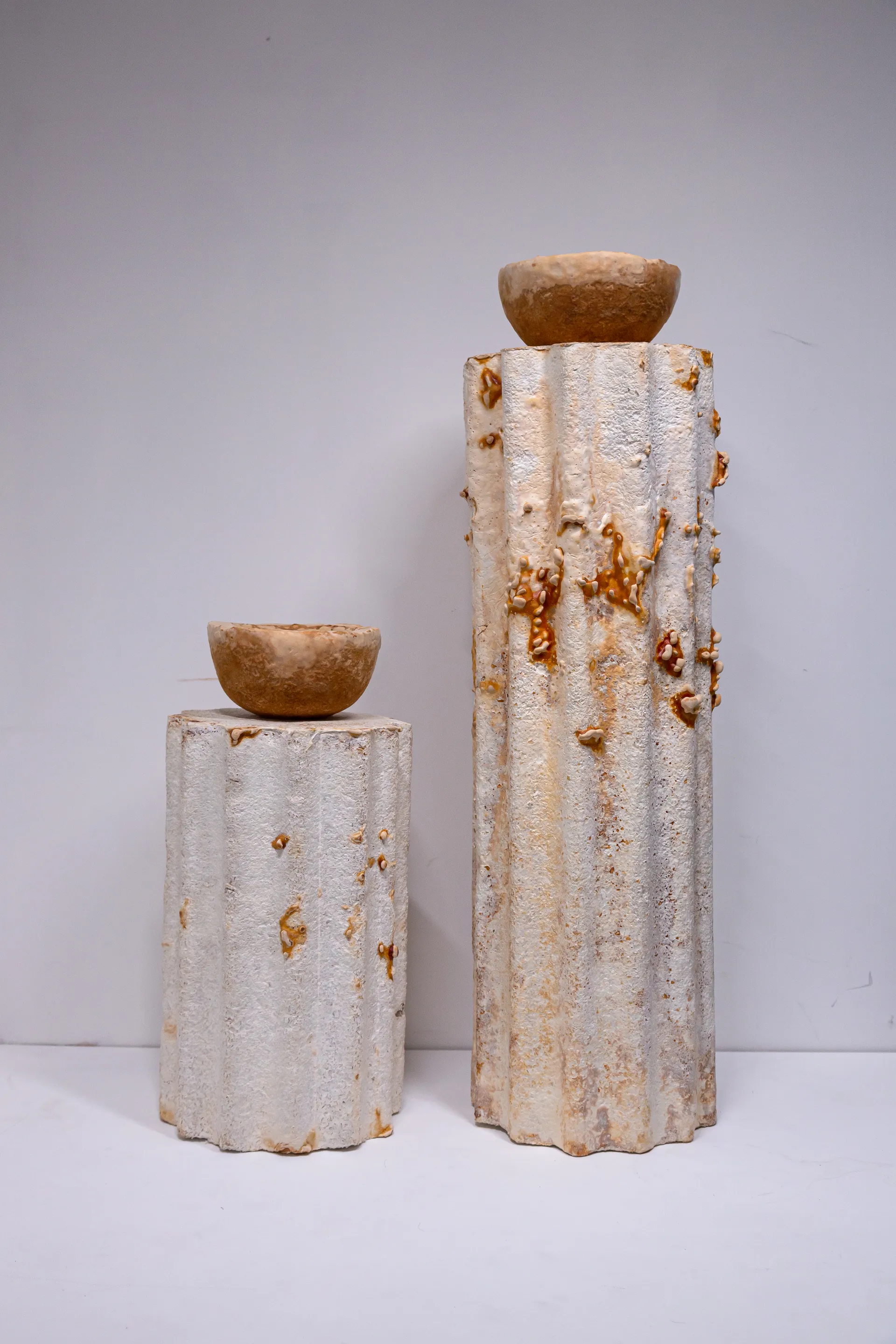 Two tall mycelium plinths displaying sculptural forms against a soft lavender backdrop